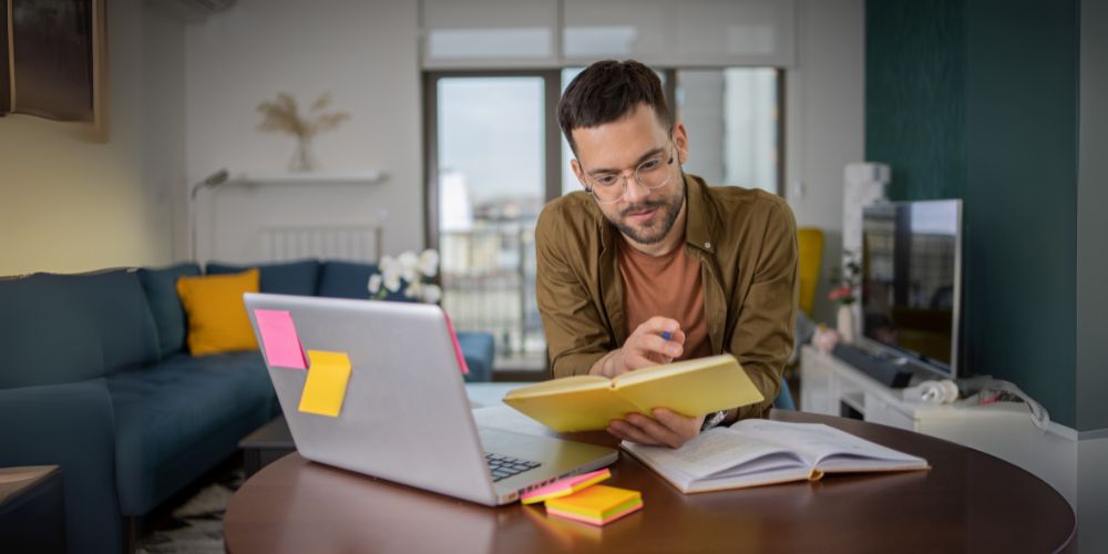 A man reading a book and using his laptop